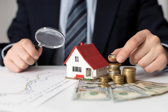 Personne en costume examinant une maison miniature avec loupe, image illustrant l’usage d’un simulateur LMNP pour évaluer rentabilité locative.