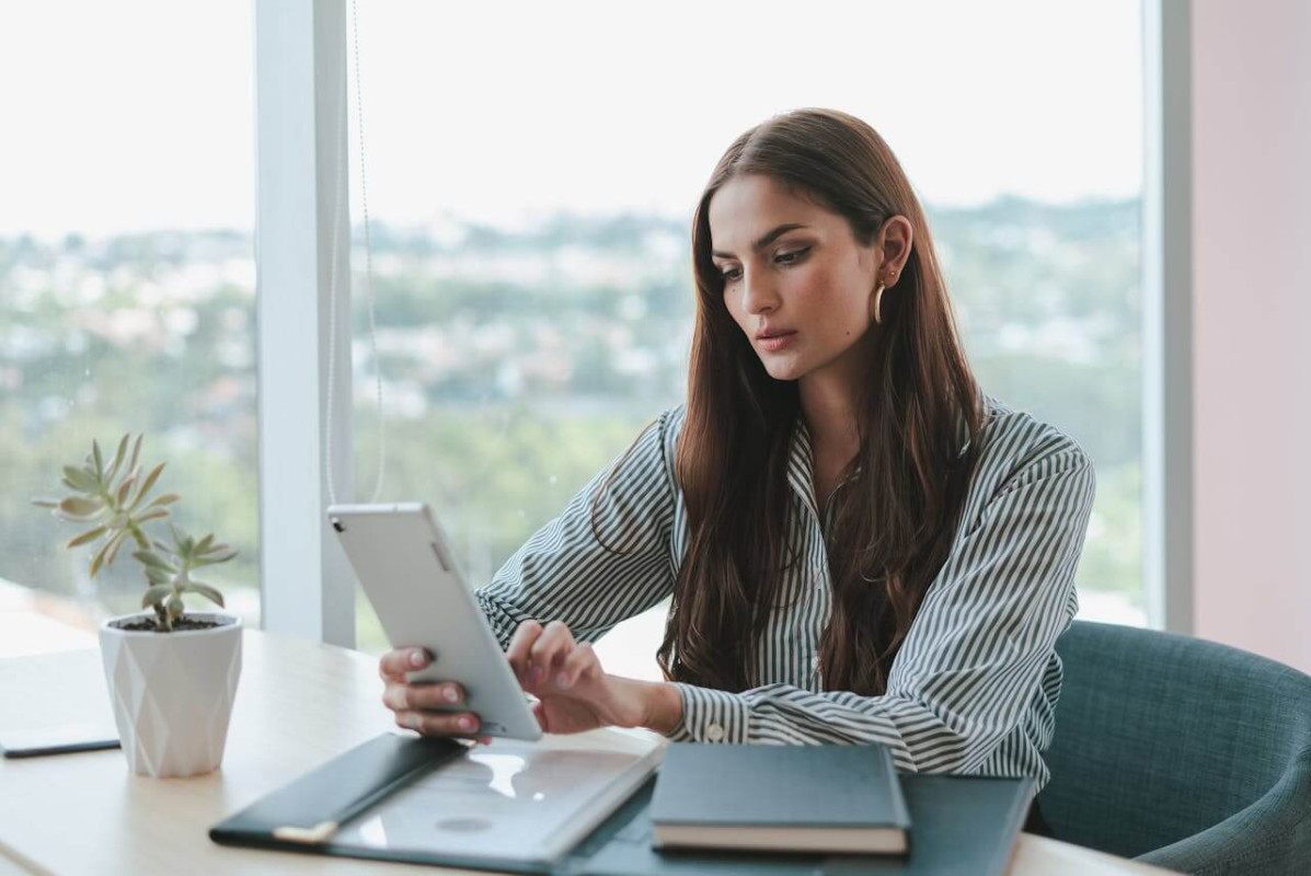 Une femme tenant des documents et utilisant une tablette, analysant les différents éléments liés au coût de création d'une SCI, tels que les frais juridiques, administratifs et fiscaux nécessaires pour monter une société civile immobilière.