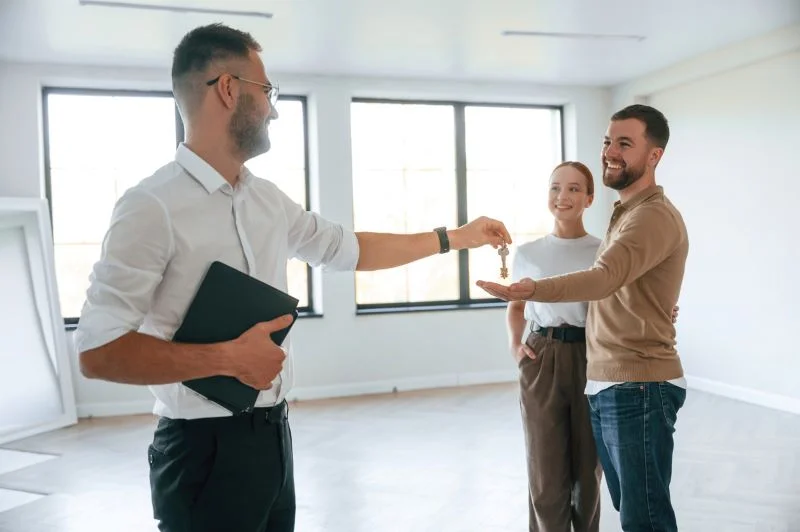 Un couple recevant d'un professionnel de l'immobilier la clé de leur logement, dans le cadre d'une location appartement Caen