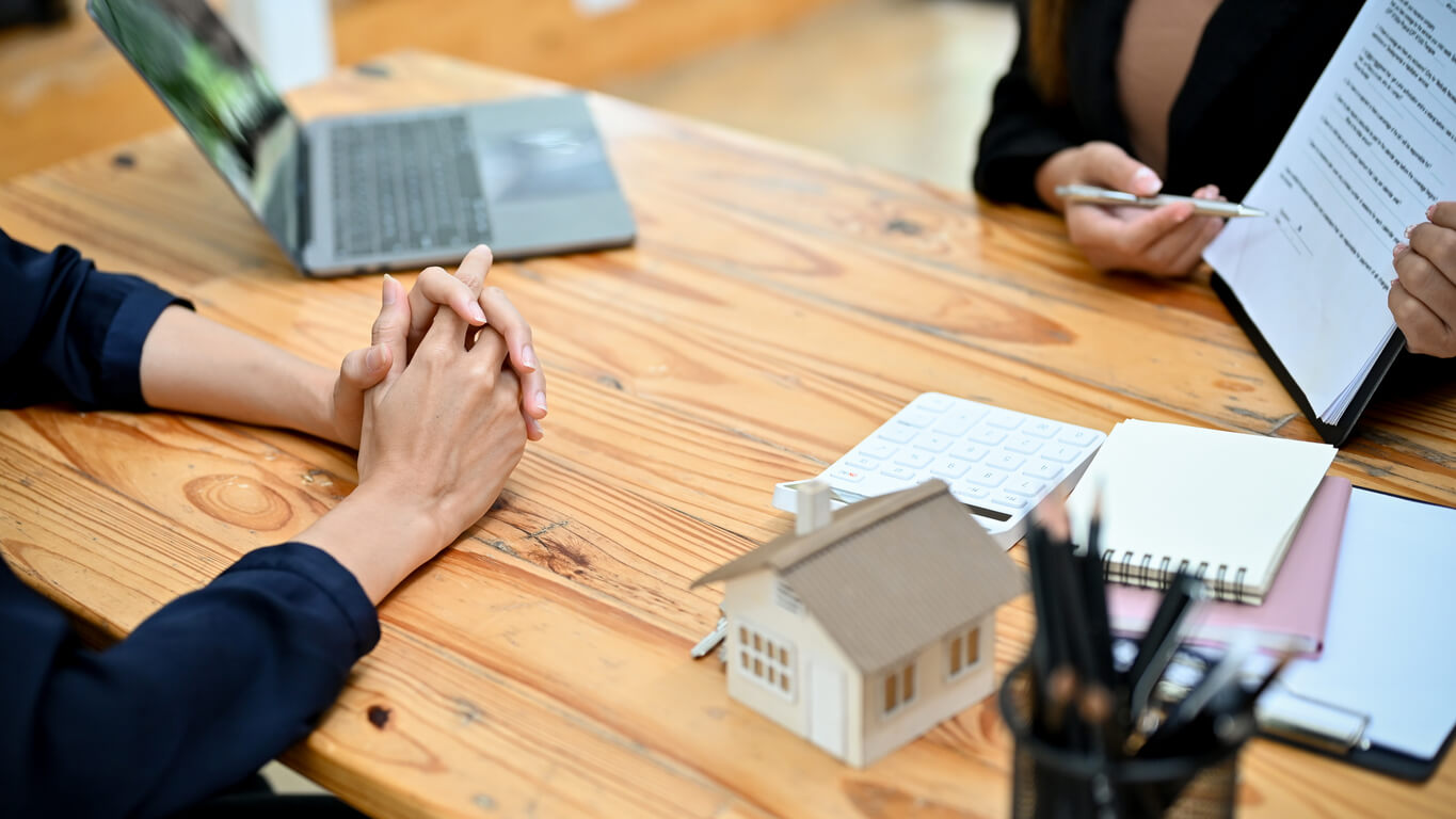 Image de deux personnes en train de discuter devant un ordinateur, avec des documents étalés sur la table, illustrant la préparation d'un dossier pour un crédit pour SCI immobilière. Cette scène reflète l'importance de bien structurer les informations et de présenter un projet solide lors de la demande de financement pour une SCI.