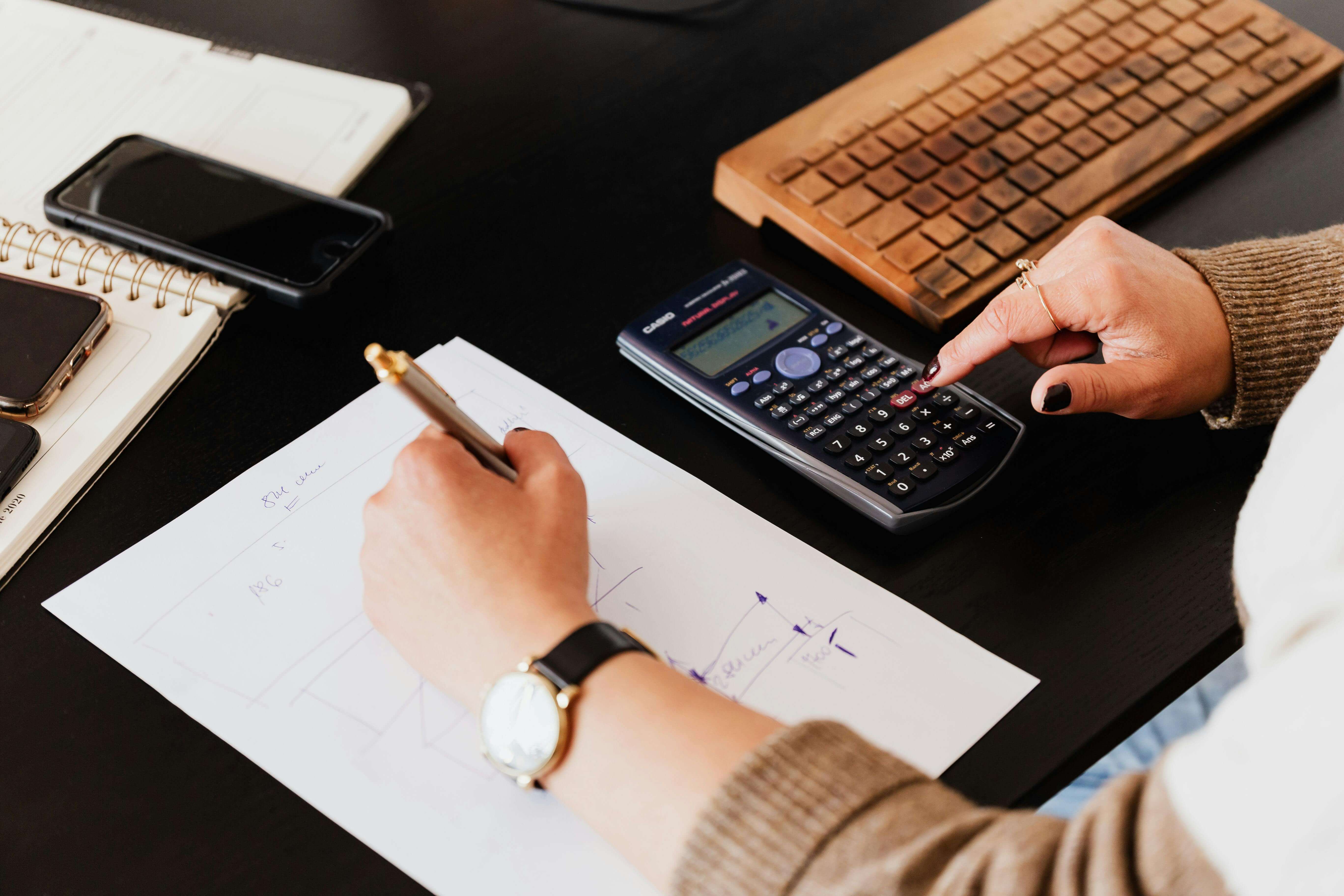 Une personne analyse des données financières avec une calculatrice et un tableau, illustrant le calcul des revenus fonciers SCI pour une gestion optimale