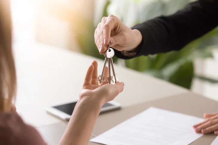 Une personne remettant à l'autre une clé. Après que les frais résiliation de gestion locative sont réglés, le gestionnaire doit remettre tout au bailleur.