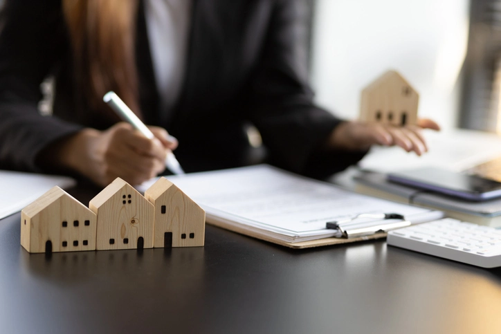  Un homme entrain d'écrire au bureau, sur lequel est aussi posé des maquettes de maison. Les professionnels maîtrisent la gestion locative Toulouse.