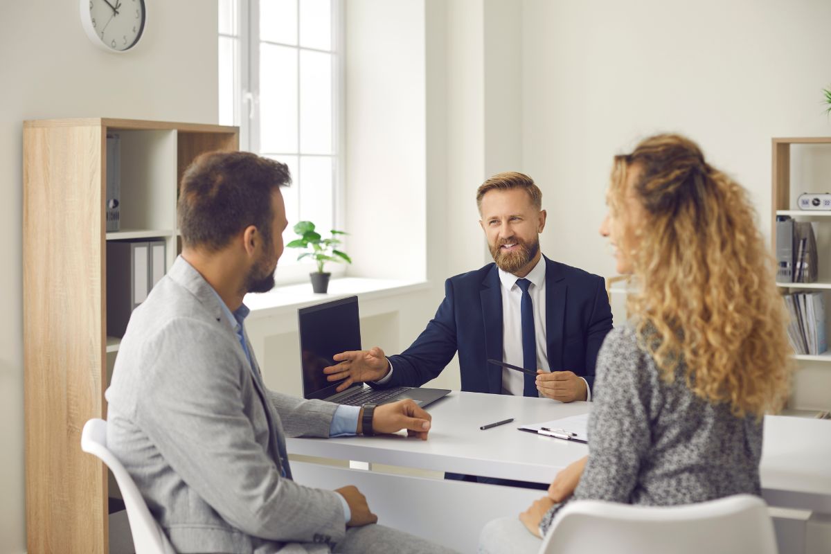 Une image de trois personnes dans un bureau, discutant pour comprendre le statut LMNP. Des documents et un ordinateur sont visibles sur le bureau, créant une ambiance professionnelle.