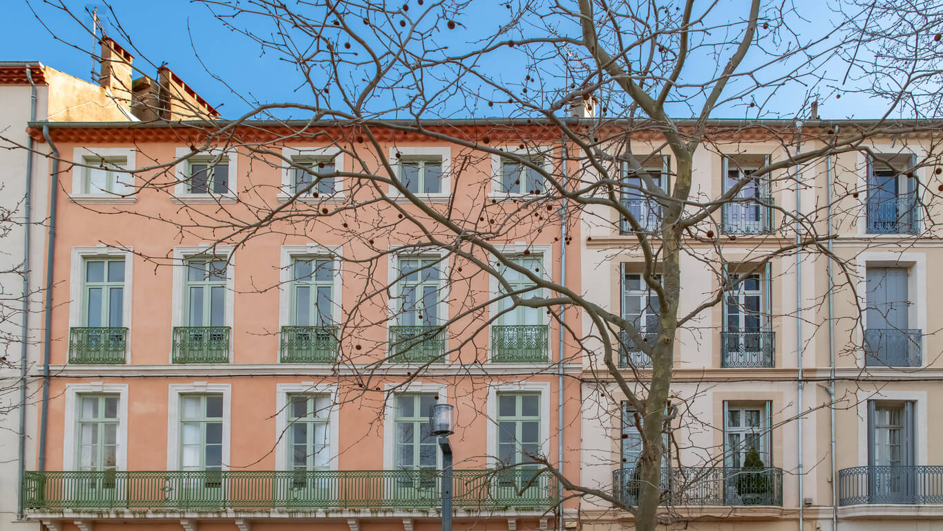 Façade colorée d'un immeuble à Béziers, avec des balcons en fer forgé vert, typique de l'architecture locale. Cette image représente un exemple de bâtiment dans le centre historique, idéal pour un investissement locatif Béziers, offrant un charme unique et un potentiel de rentabilité élevé.