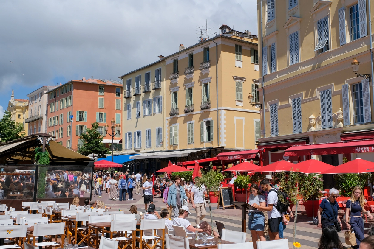 Rue animée avec terrasses de cafés et immeubles colorés à Nice, Côte d'Azur, une région prisée pour investir dans l'immobilier en bord de mer.