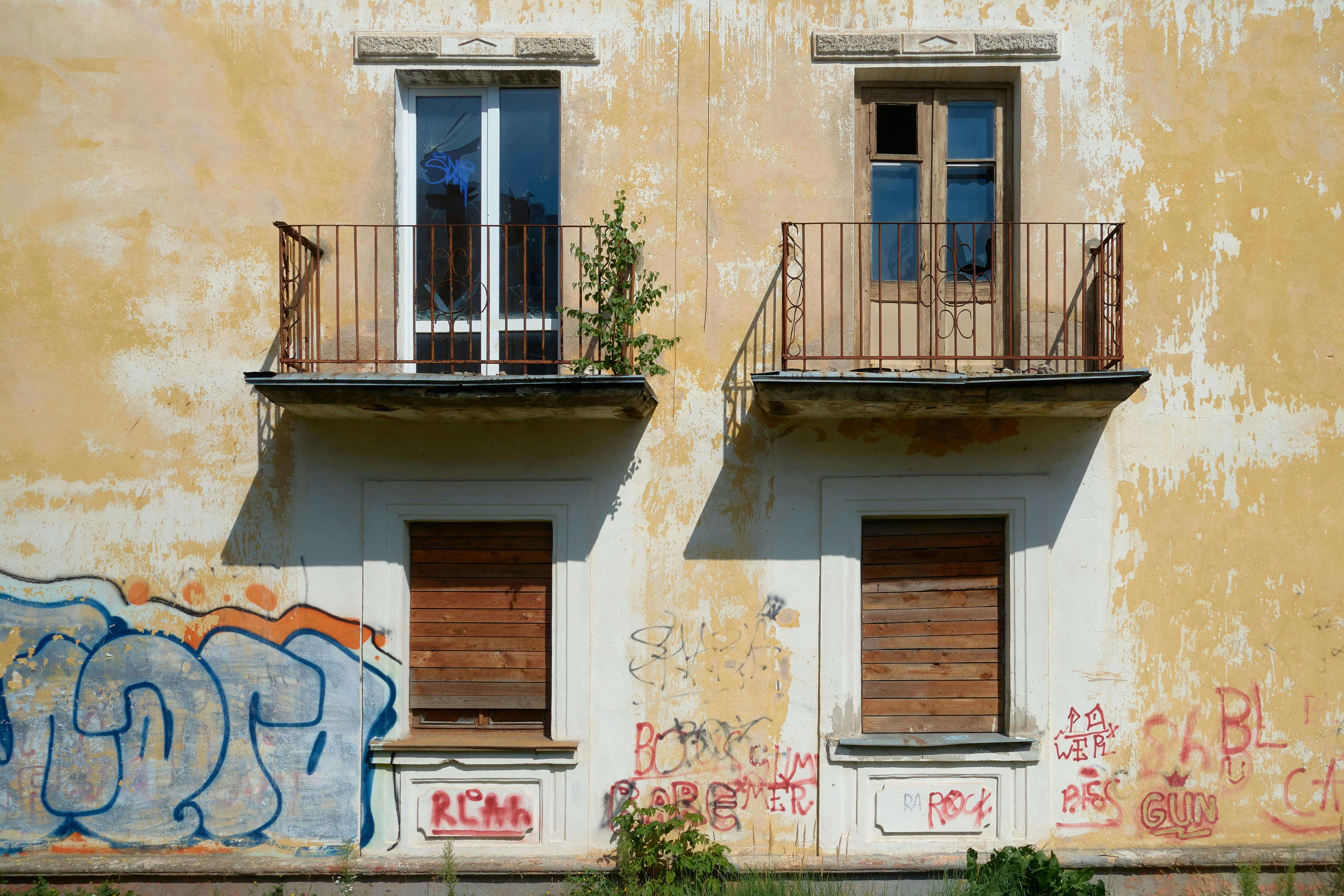 Façade d'une maison ancienne à rénover, avec balcons rouillés et graffitis, offrant un potentiel intéressant pour un investissement locatif Alès après travaux