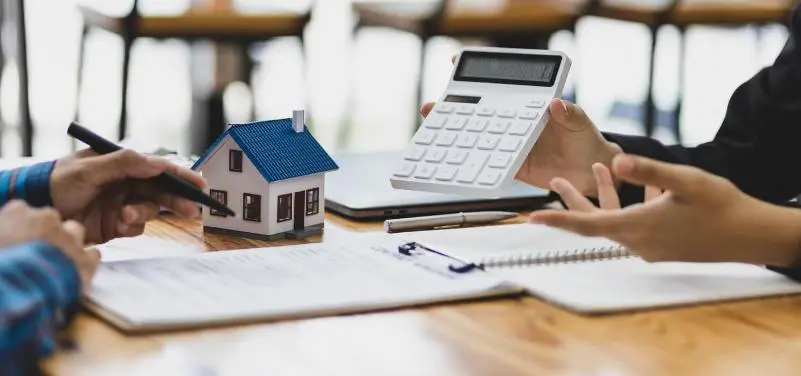 Deux personnes assises au bureau, dont l'une montre à l'autre une calculatrice montrant les frais de gestion locative, un élément clé avant la signature du contrat.