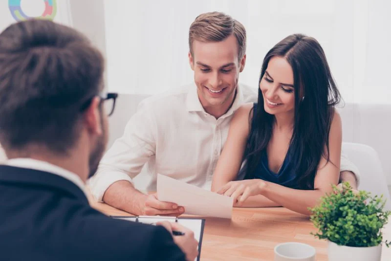 Un couple devant un professionnel au bureau, vérifiant les critères de choix du nouveau responsable dans le cadre d'un changement de gestion locative en cours de bail.