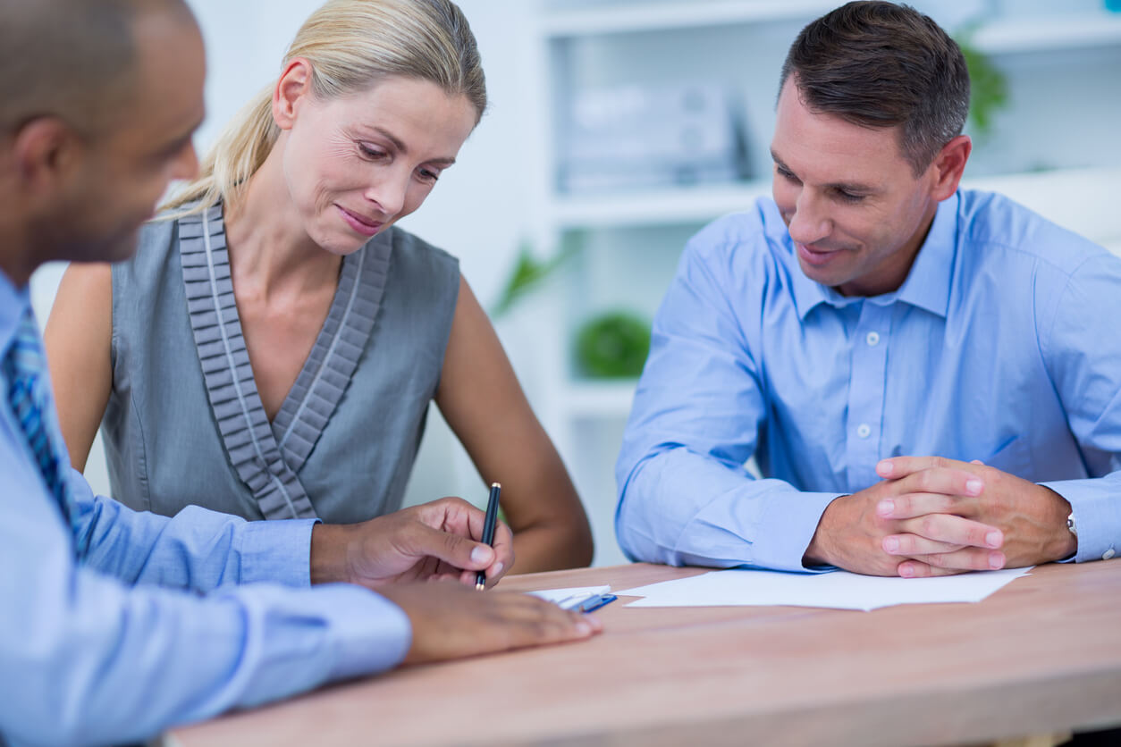 Trois personnes discutent autour d'une table, dont une qui signe des documents liés au rachat d'une assurance-vie, mettant en lumière les implications fiscales de cette démarche.