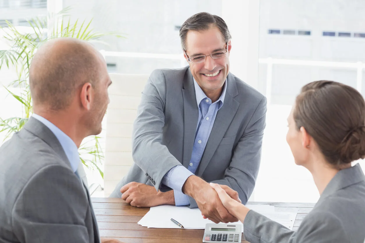 Un couple et un gestionnaire immobilier discutent d'un contrat de location devant un bien immobilier.