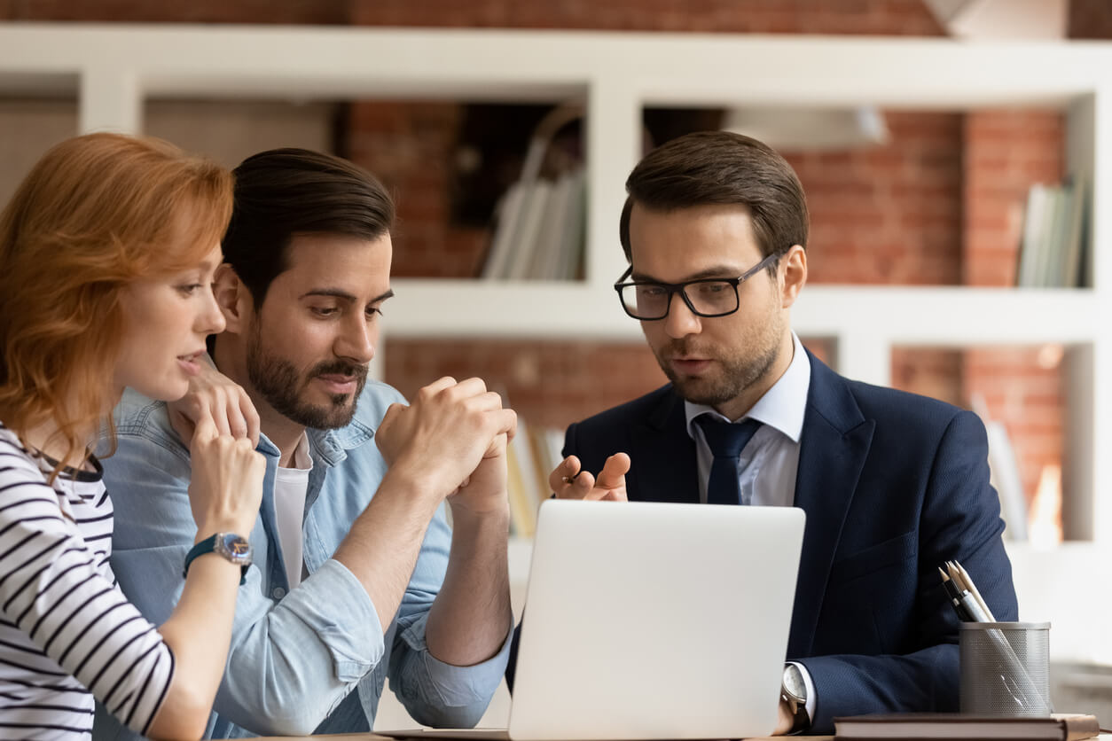 Image de trois personnes au bureau avec des dossiers, discutant des facteurs influençant le taux emprunt SCI 20 ans, tels que la capacité d'emprunt, les conditions de marché et le projet immobilier.