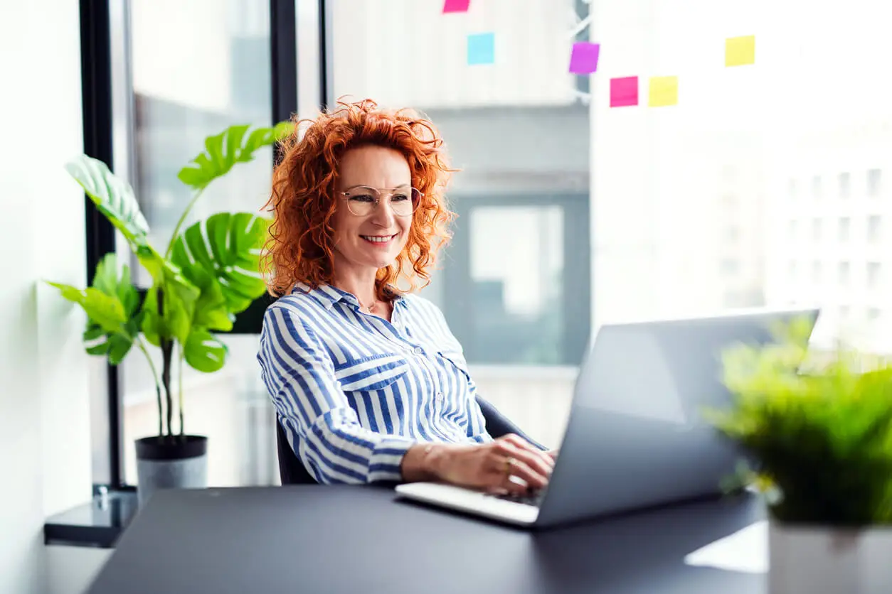 Une femme assise à son bureau, concentrée devant son ordinateur, examinant les détails financiers et administratifs liés au coût de création d'une SCI (Société Civile Immobilière), incluant les frais de notaire, d'expertise et de formalités légales.